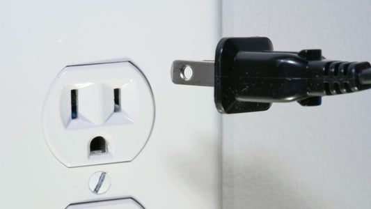 Close-up of a black electrical plug about to be inserted into a white wall outlet
